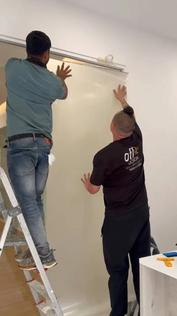 Two Smart Glass Solution technicians in Offix shirts hanging switchable film onto an existing glass panel on site in Singapore