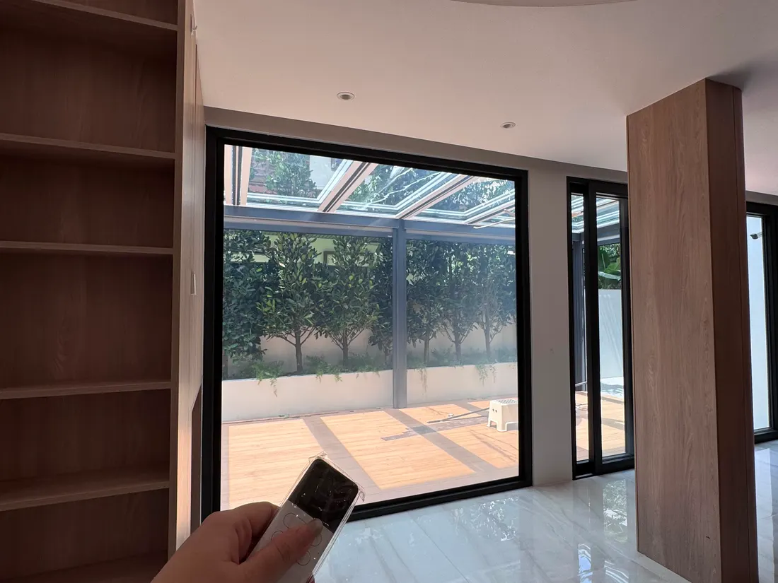 A residential living space with the glass wall switched clear to the garden, remote in hand