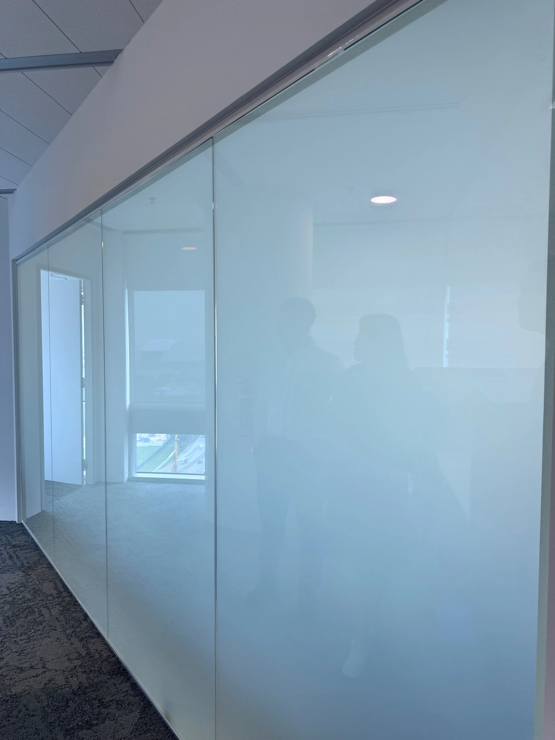 The same office glass partition with smart film in private mode, frosted so only soft silhouettes remain visible