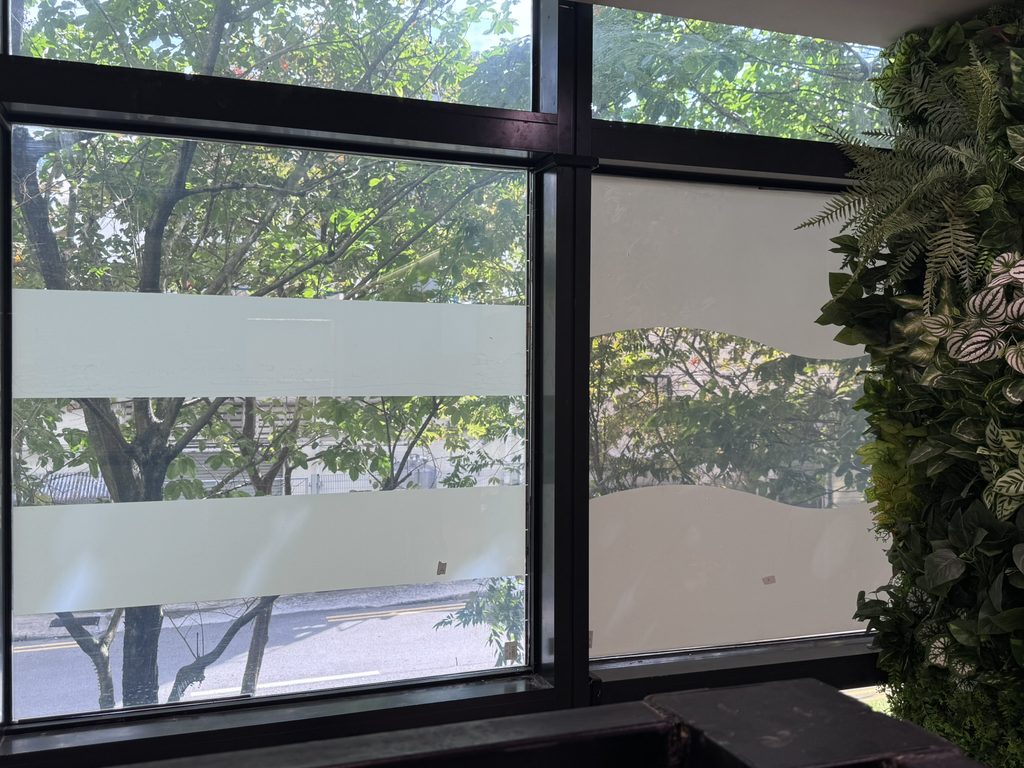 Frosted privacy bands applied across office windows, screening the view at eye level while keeping the greenery visible above and below